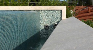 Elementi in travertino e mosaico per il progetto di questa piscina a sfioro sul tetto.